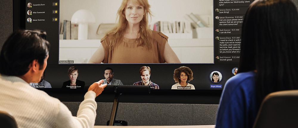 Two people in a conference room participating in a video call with six remote attendees