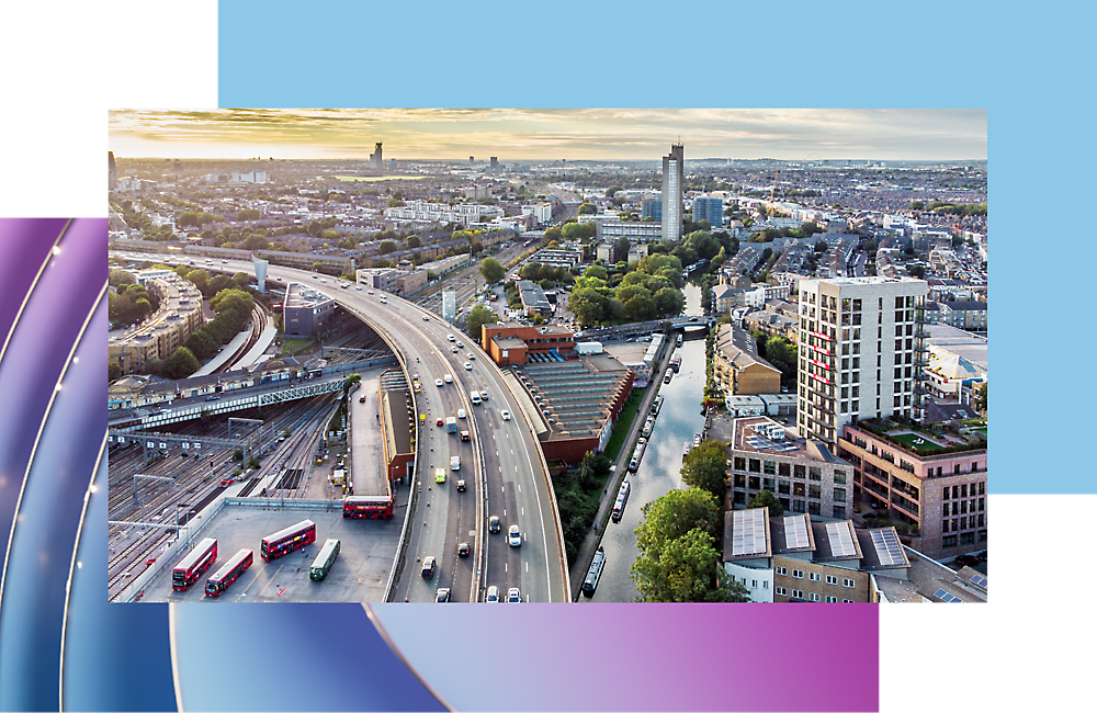 Aerial view of a busy city highway with multiple lanes and red buses, surrounded by modern buildings.