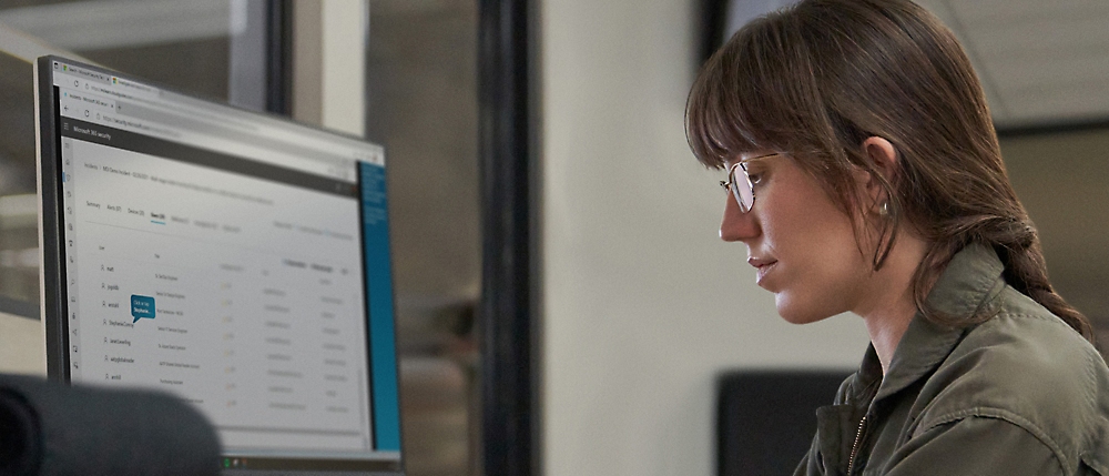 Woman with glasses focusing on a computer screen displaying software code, in an office environment.