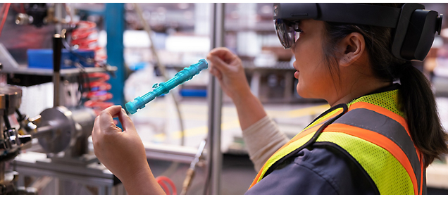 Um trabalhador com um colete de segurança e óculos de realidade aumentada inspeciona um componente industrial.