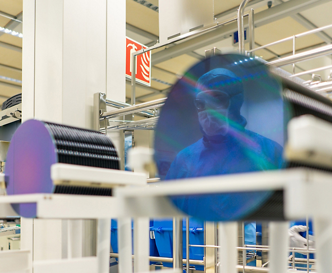 A technician in cleanroom attire inspects semiconductor production in a high-tech facility.