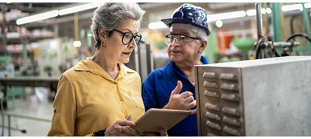 Senior factory supervisor with tablet discussing production details with a worker.