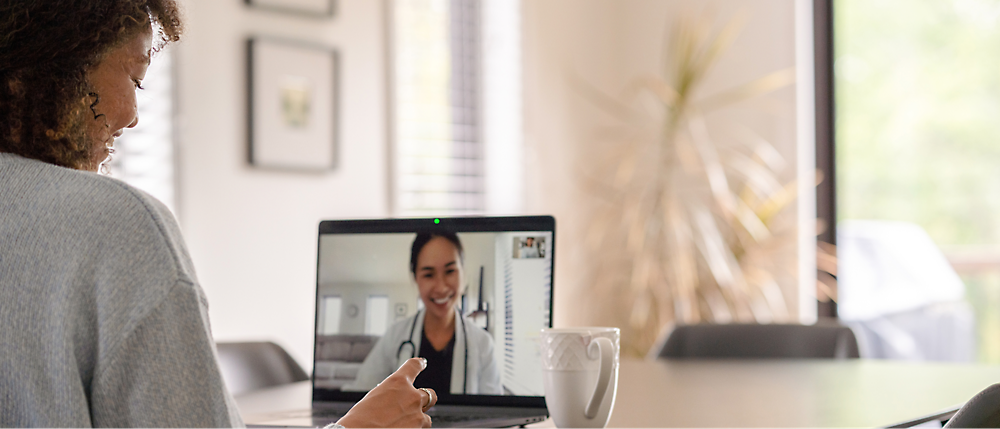 A woman is sitting in front of computer screen and in a video call with a doctor