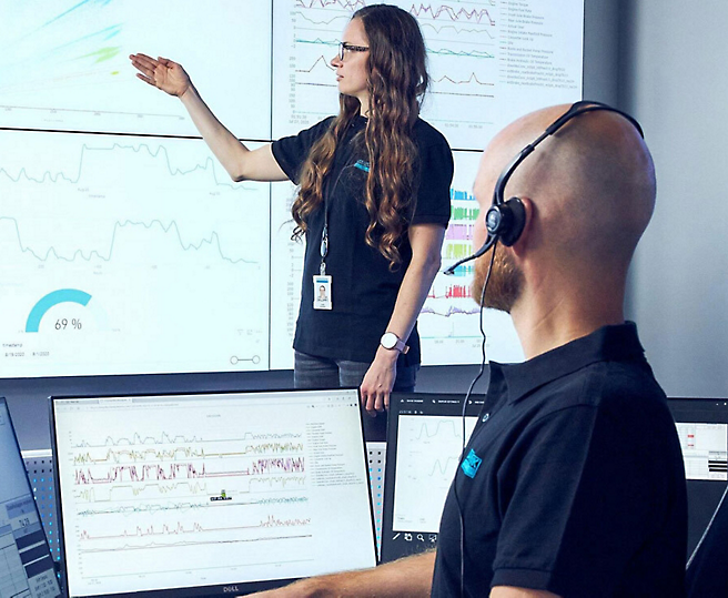 Um soldador com equipamento de proteção foca-se no seu trabalho à medida que as faíscas voam do metal que está a moer. Uma mulher aponta para dados num monitor enquanto um homem com auscultadores olha para um ecrã de computador.