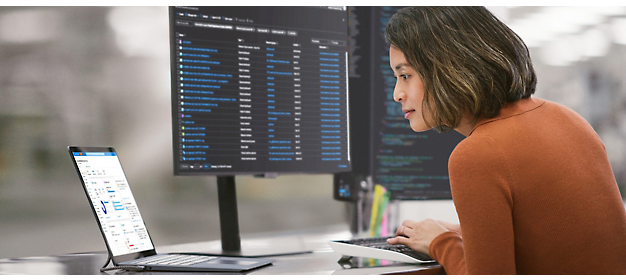 Woman analyzing data on computer screens in an office setting.