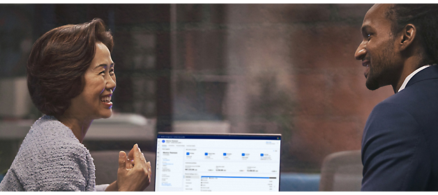 Two professionals engaging in a discussion with a laptop displaying data on the desk between them.