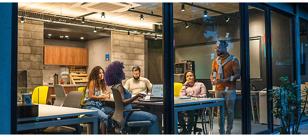 Four individuals in a modern office space during an evening meeting, with one person presenting.