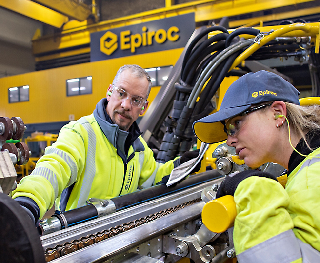 Dois técnicos com coletes de alta visibilidade a trabalhar em máquinas industriais numa instalação da Epiroc.