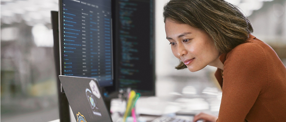 A woman concentrates on coding on her computer in a modern office setting.