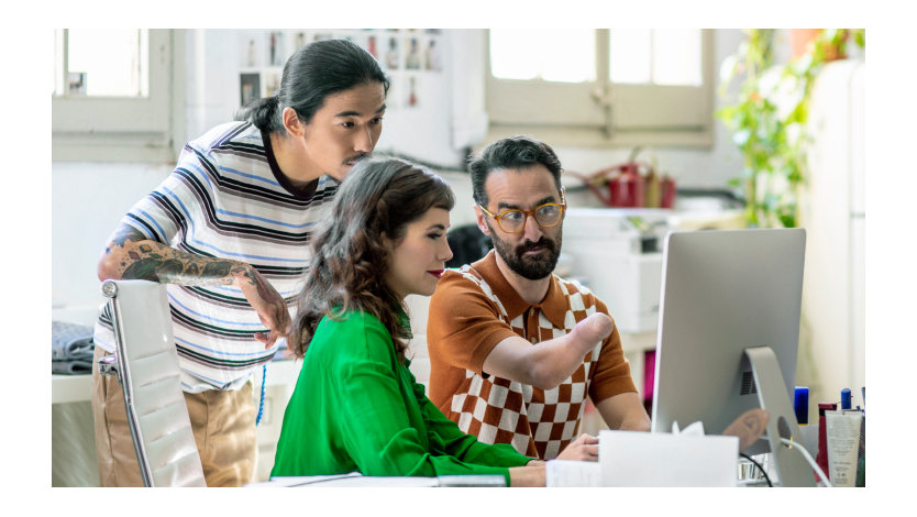 In an office, three people, one of whom has a physical disability, look at a monitor.