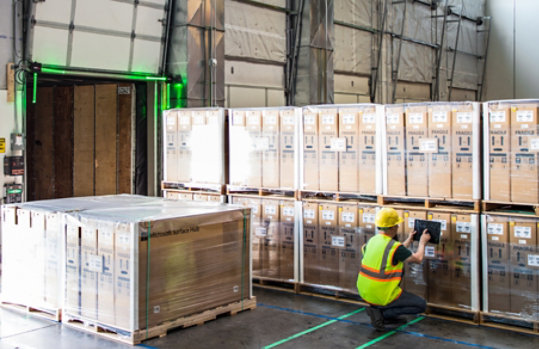 Man in safety gear using a tablet while checking crates in a warehouse.