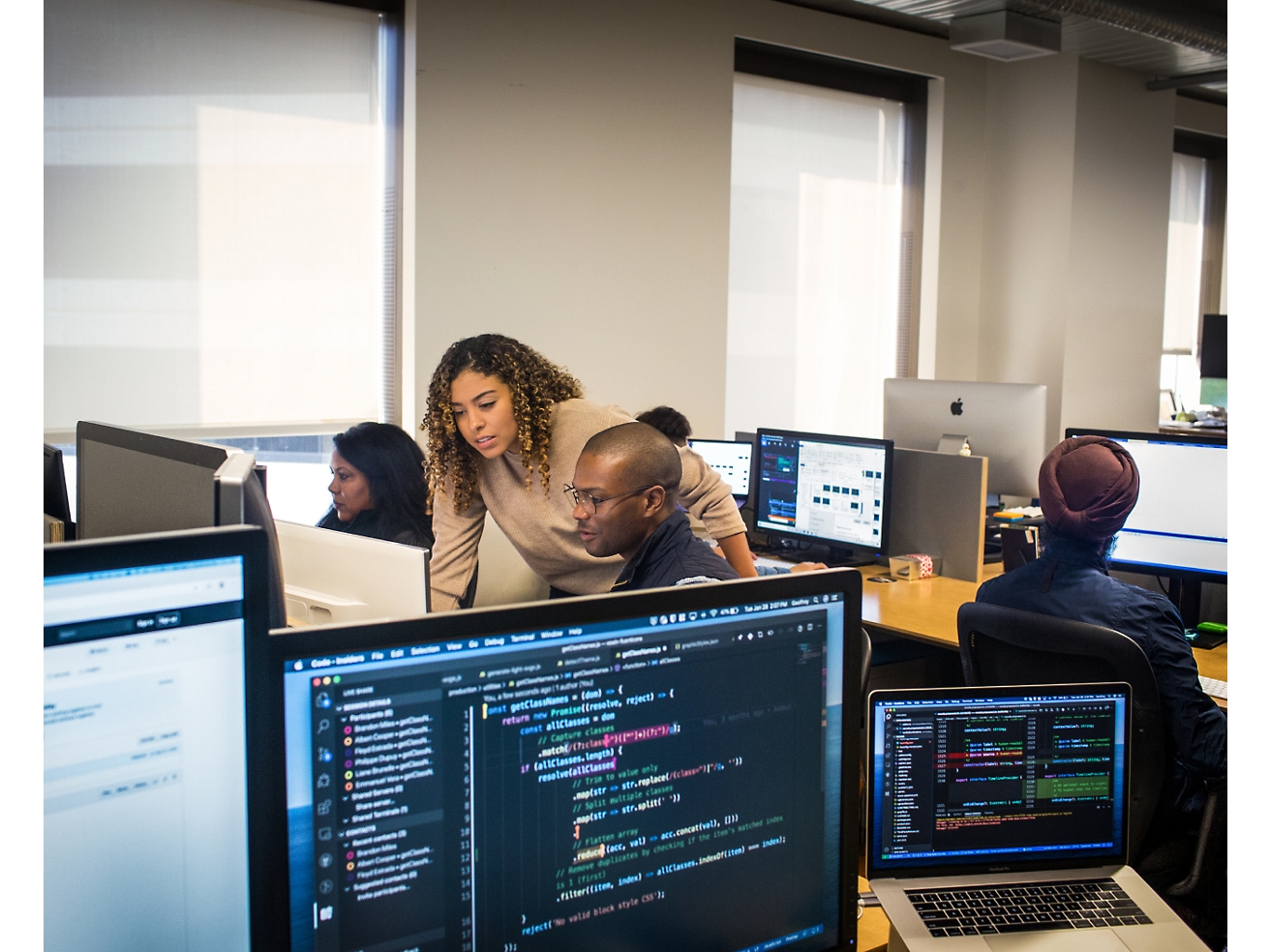 在辦公環境中使用電腦的不同專業人員群組，專注於可看見各種程式碼和資料的螢幕。