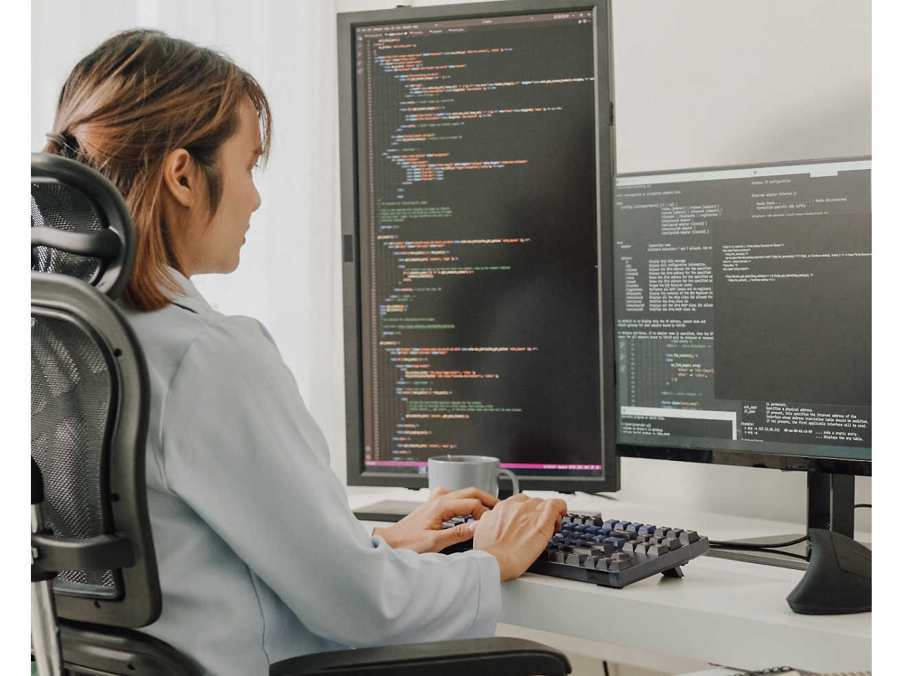 一個女人坐在辦公椅上，在電腦上編寫程式碼，電腦上有多個螢幕顯示了程式碼。