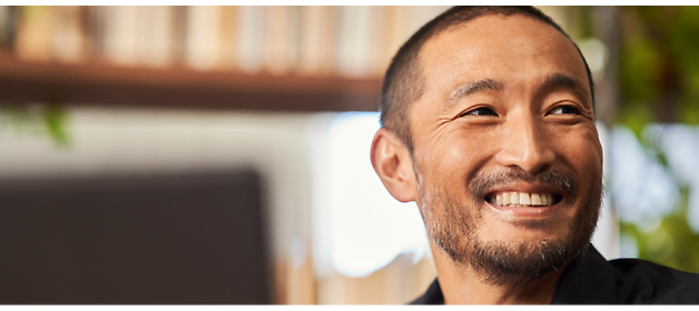 A man with a short beard and close-cropped hair smiles while looking to his left, with shelves 