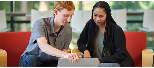 Two people sitting on red chairs, collaborating while looking at a laptop screen