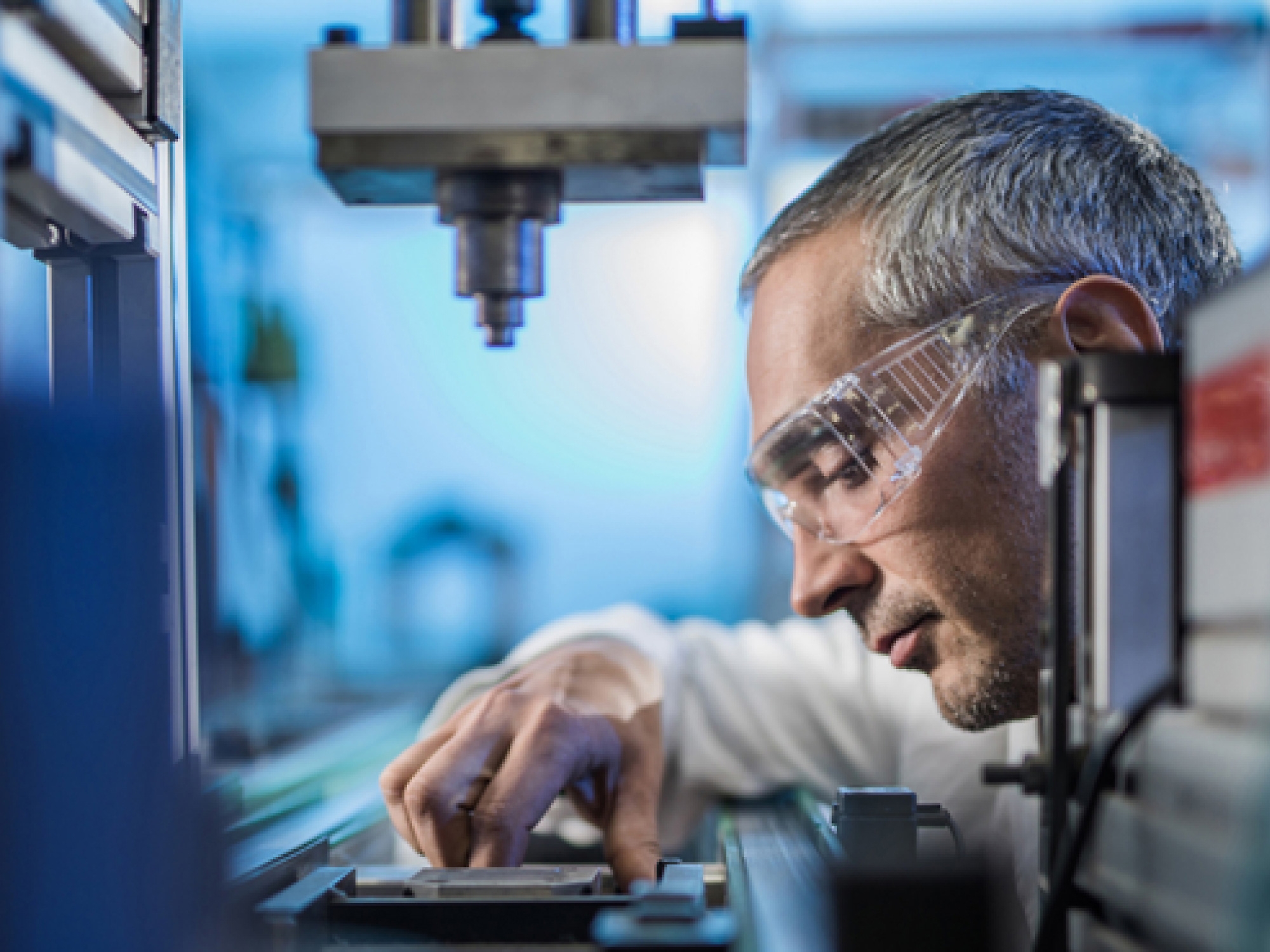 Um técnico com óculos de proteção ajusta cuidadosamente o equipamento num laboratório.