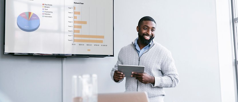 Ein Mann, der vor einem TV-Gerät steht und ein Tablet vor sich hat