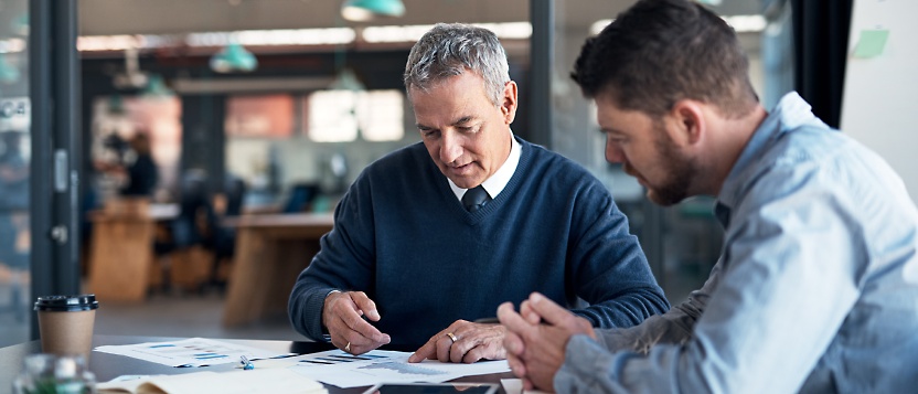 Two men sitting at a table looking at papers.