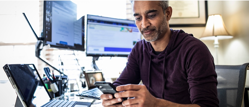 Ein Mann, der an seinem Schreibtisch sitzt und sein Smartphone benutzt