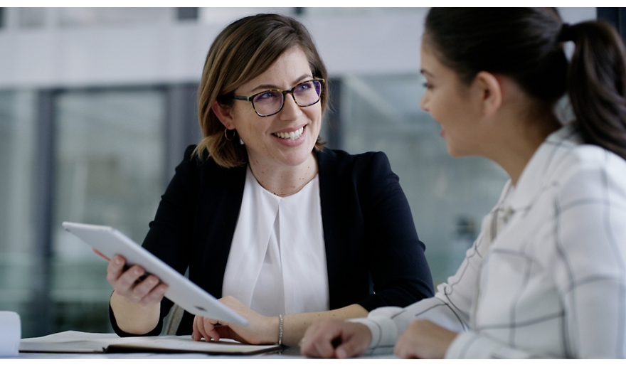 Two business women talking at a table with a tablet.