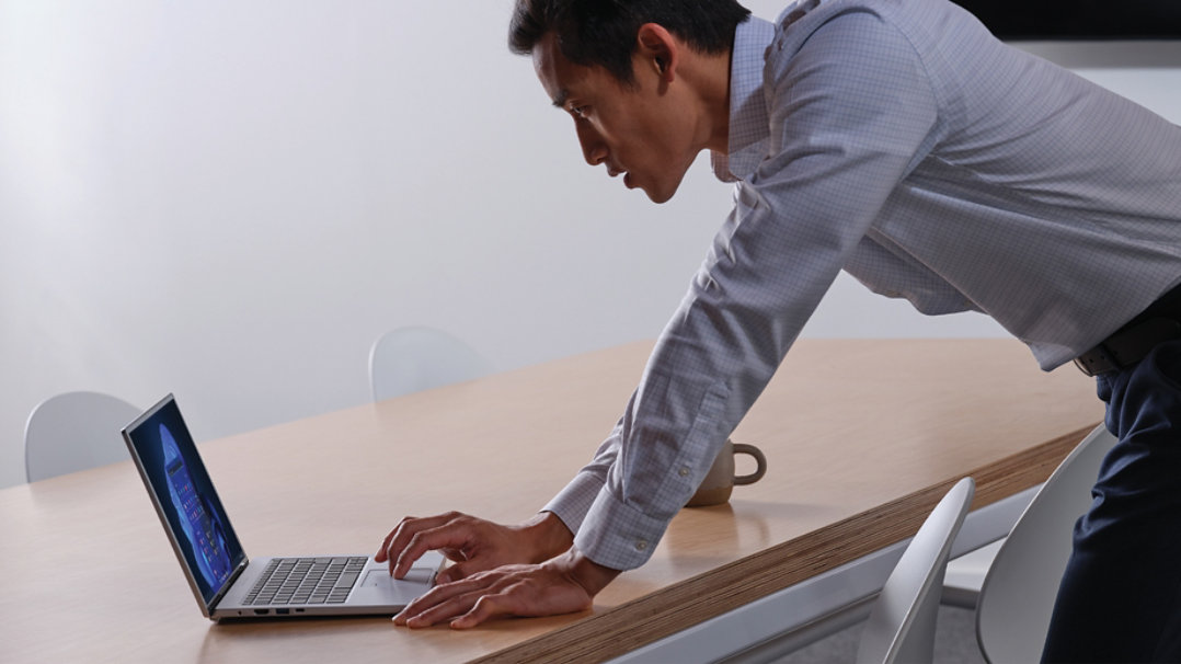 A man leaning over a table while  using a laptop