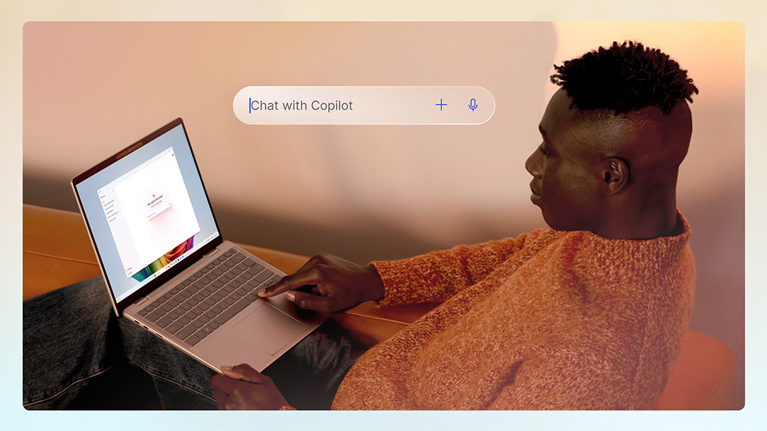 A man lounging on an orange couch using the Copilot chat window on his laptop