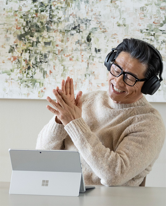 Un hombre sonriente, con cascos, sentado en una mesa delante de un dispositivo Surface