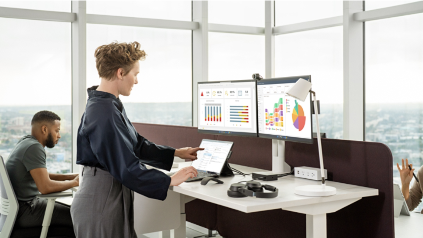 A person working on a Surface device with two monitors in glassy office