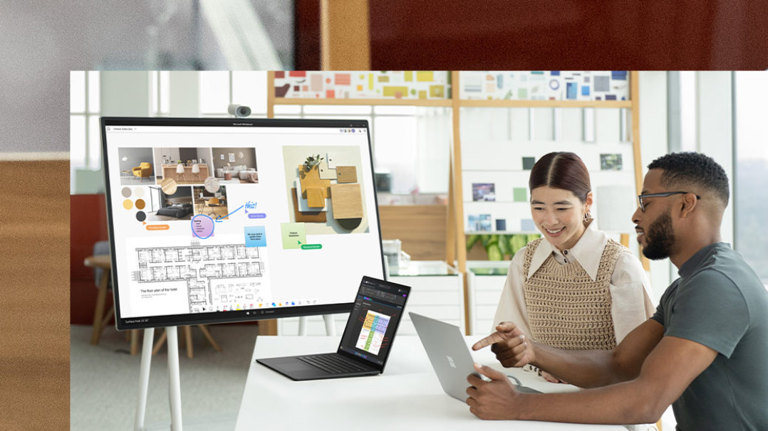 Two coworkers interact with two Surface Laptop 5 devices with a Hub 2S in the background