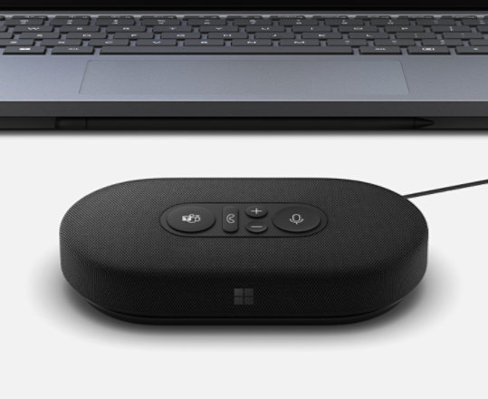 A render of a Microsoft Modern USB-C Speaker plugged into a Surface device in the background