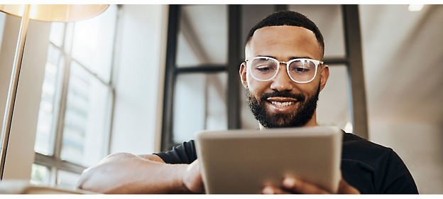 A man is wearing glasses, black tee, holding a tablet and smiling.