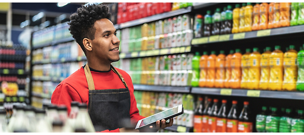 An stock clerk is using a tablet and looking at the shelves.