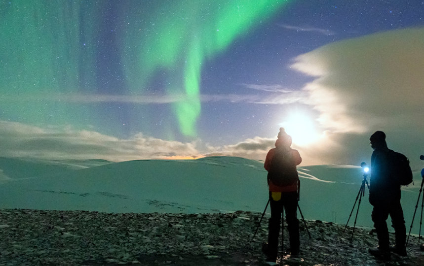 Three people with cameras photographing the northern lights on a cold winter night in Northern Norway.