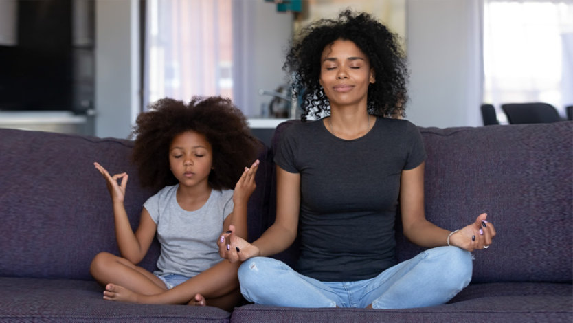 Photo credit: fizkes/iStock/Getty Images. Mother and young daughter doing yoga together at home on their couch