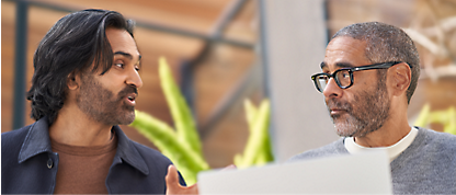 Two men talking to each other while using a laptop.