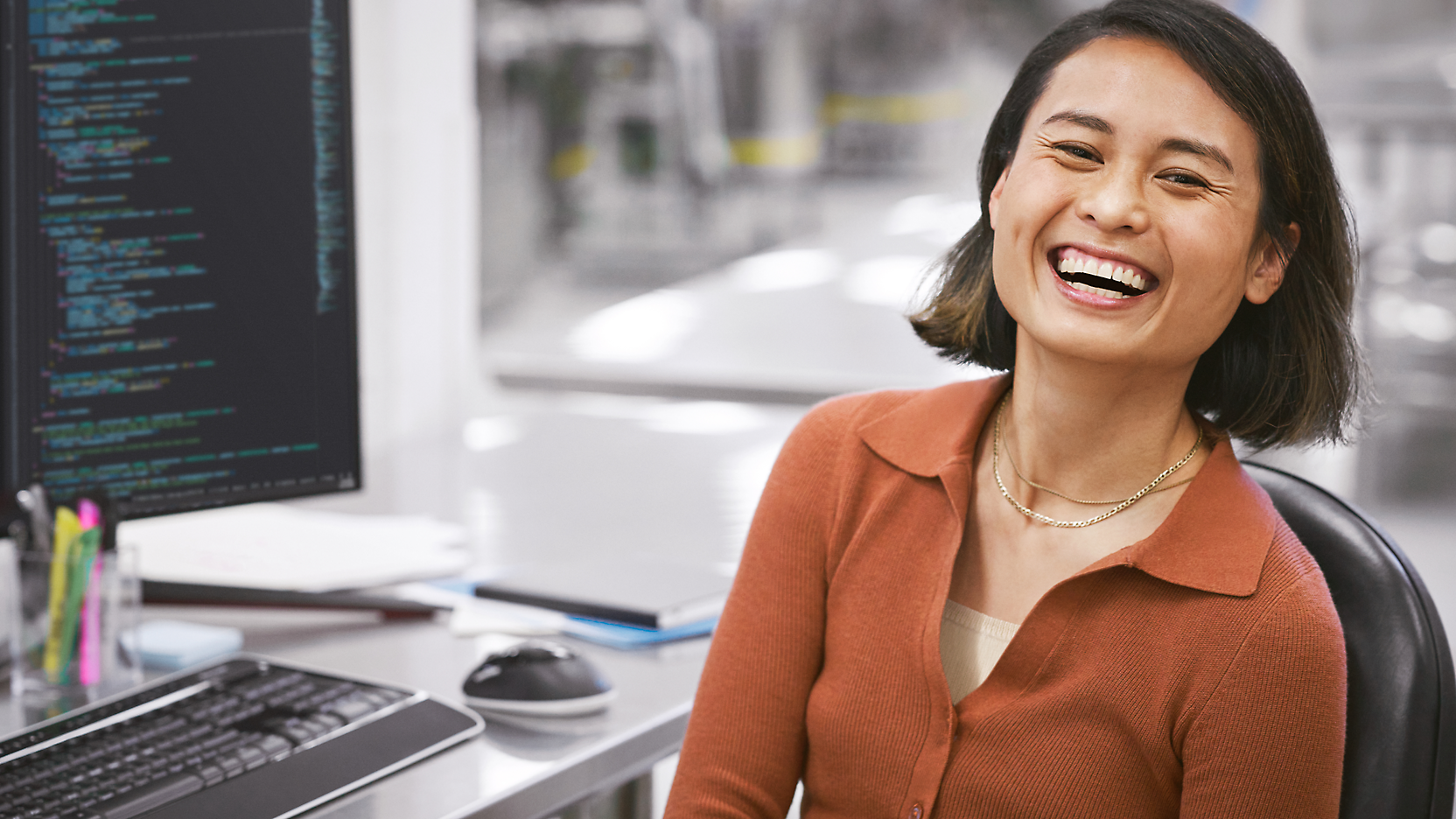 在現代辦公環境中，一位快樂的女人坐在桌前，桌上有一台電腦，螢幕上顯示著程式碼。