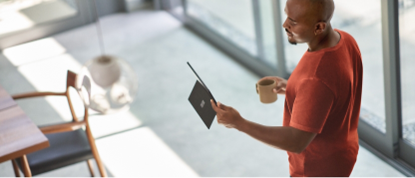 A man is holding a tablet in front of a window.