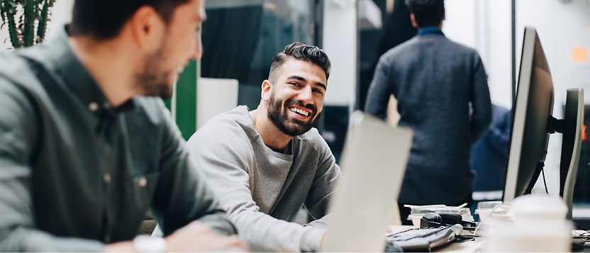 Eine Gruppe von Personen im Büro, die sich unterhalten und an den Desktops arbeiten