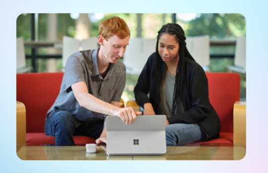 Twee studenten kijken naar het scherm van een platina Surface-computer. Een lichtgrijze Surface Arc-muis ligt op de tafel. 