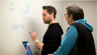 Two people talk while one of them writes on a whiteboard.