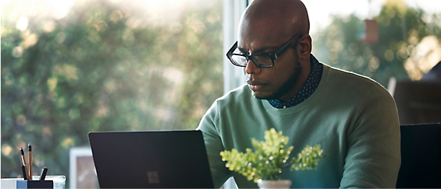 A man working on a laptop in front of a window.