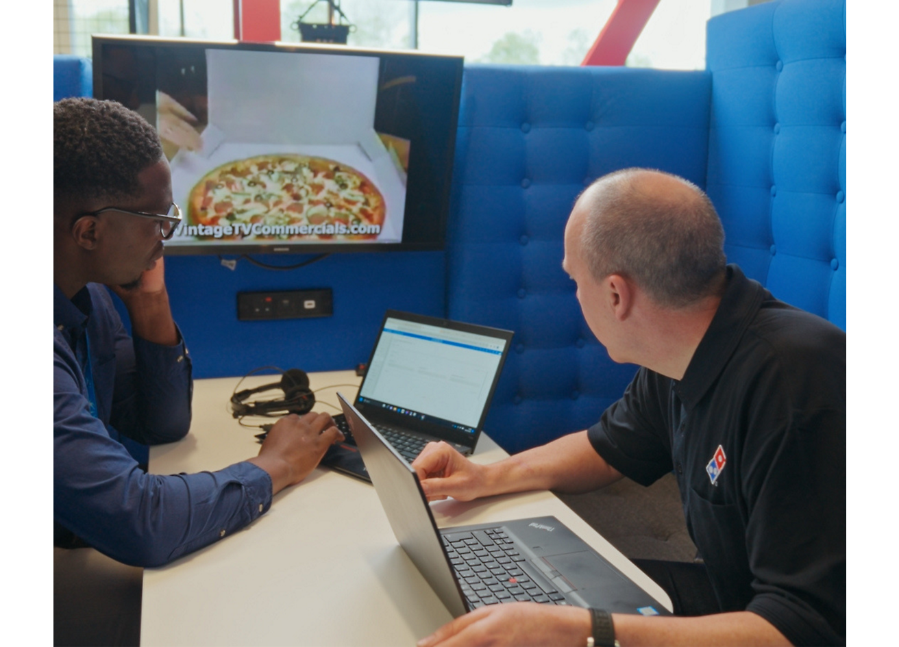 兩個人坐在膝上型電腦旁討論 Dominos Pizza