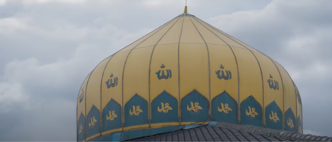 影像中顯示多雲天空下裝飾著阿拉伯文字的清真寺圓頂。