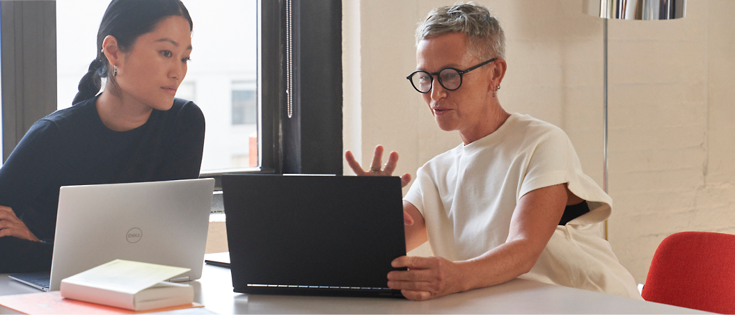 Two people sit at a table, each with a laptop in front of them.