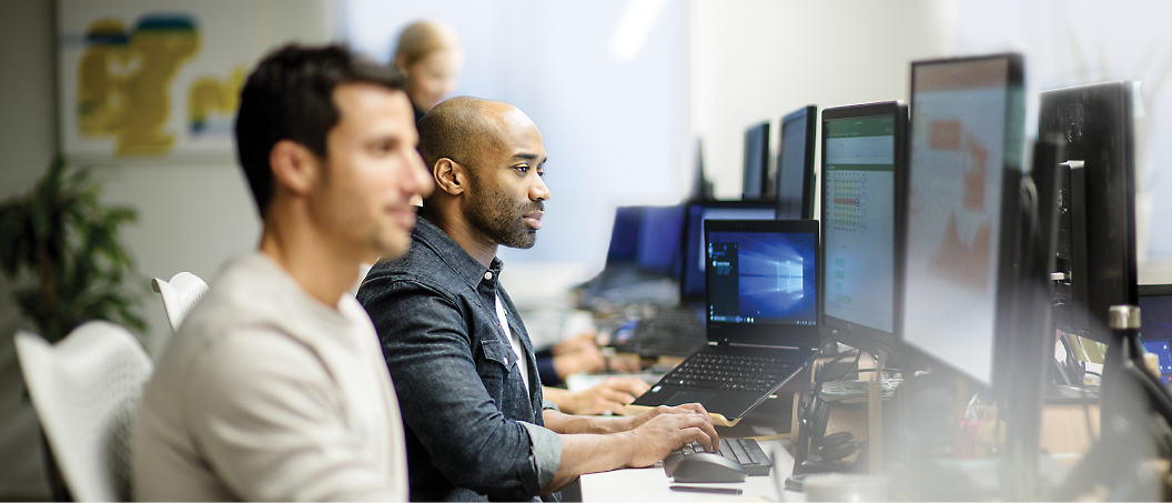 People working on laptops and desktop computers in an office setting.