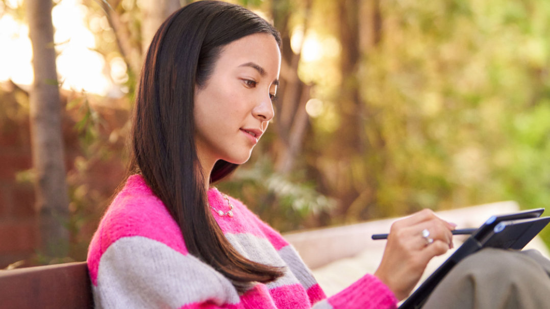 Een vrouw op een bankje in het park die een digitale pen op haar pc gebruikt