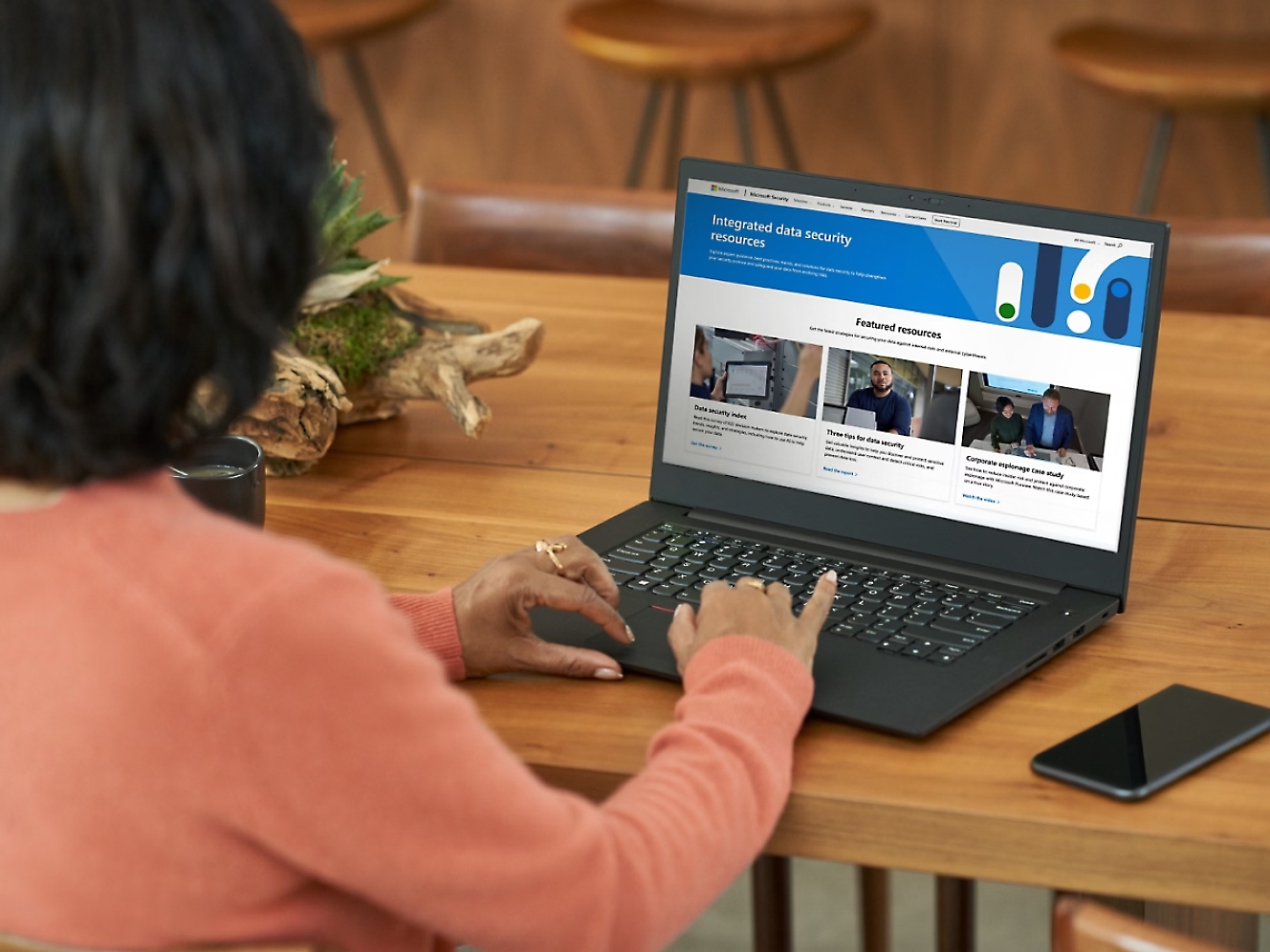 膝上型電腦身穿橙色毛衣的女士使用膝上型電腦，在木桌上的螢幕上顯示有關資料安全性的網站