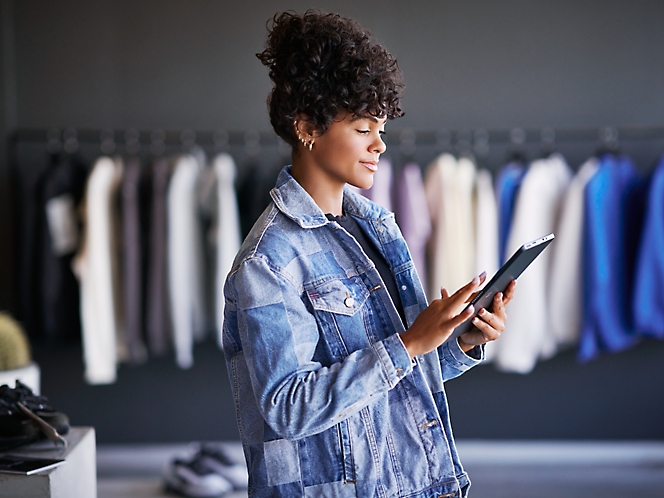 A woman in a clothing retail store working on her tablet.