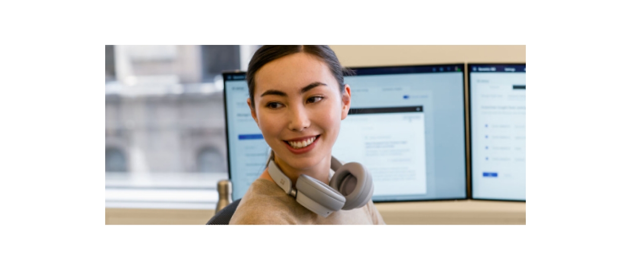 A woman wearing headphones in front of two monitors.