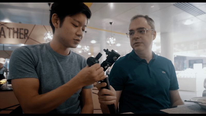 Two people having a conversation while working on a long arm-like contraption.